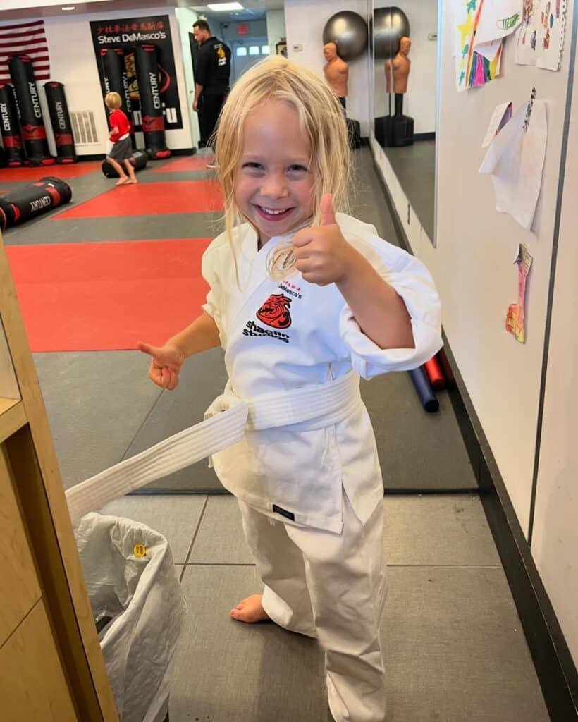 Girl in karate uniform smiling and giving a thumbs up sign
